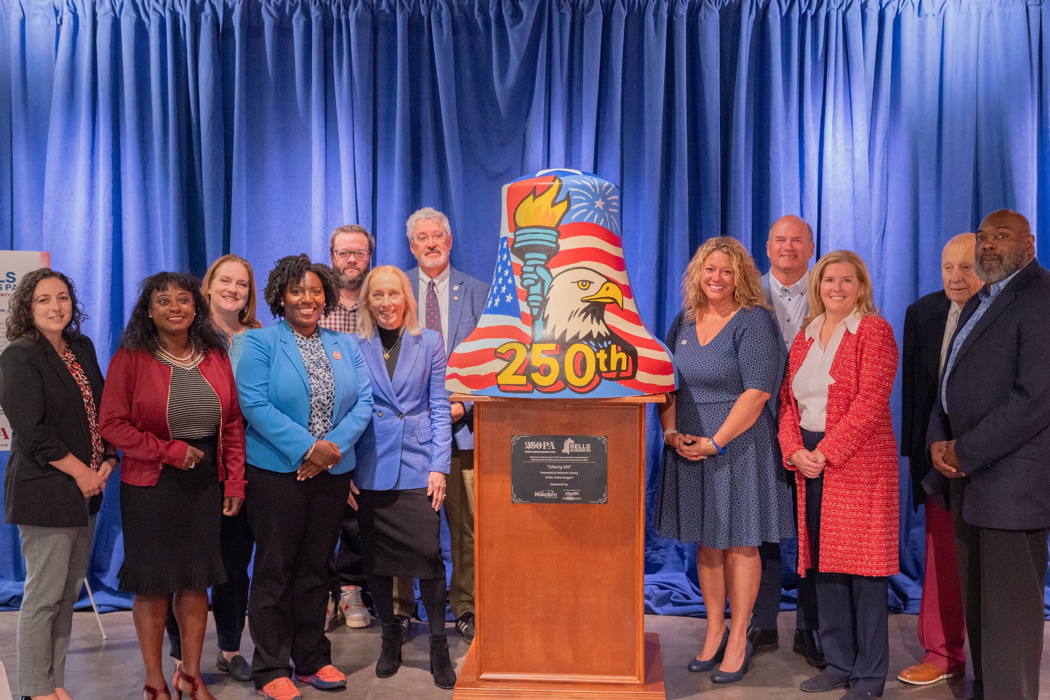 Group of 12 gather around a painted Bell at the America250PA Bell unveiling at ShopRite of Drexeline